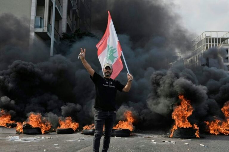 A protester holds a flag in front of burning tires.